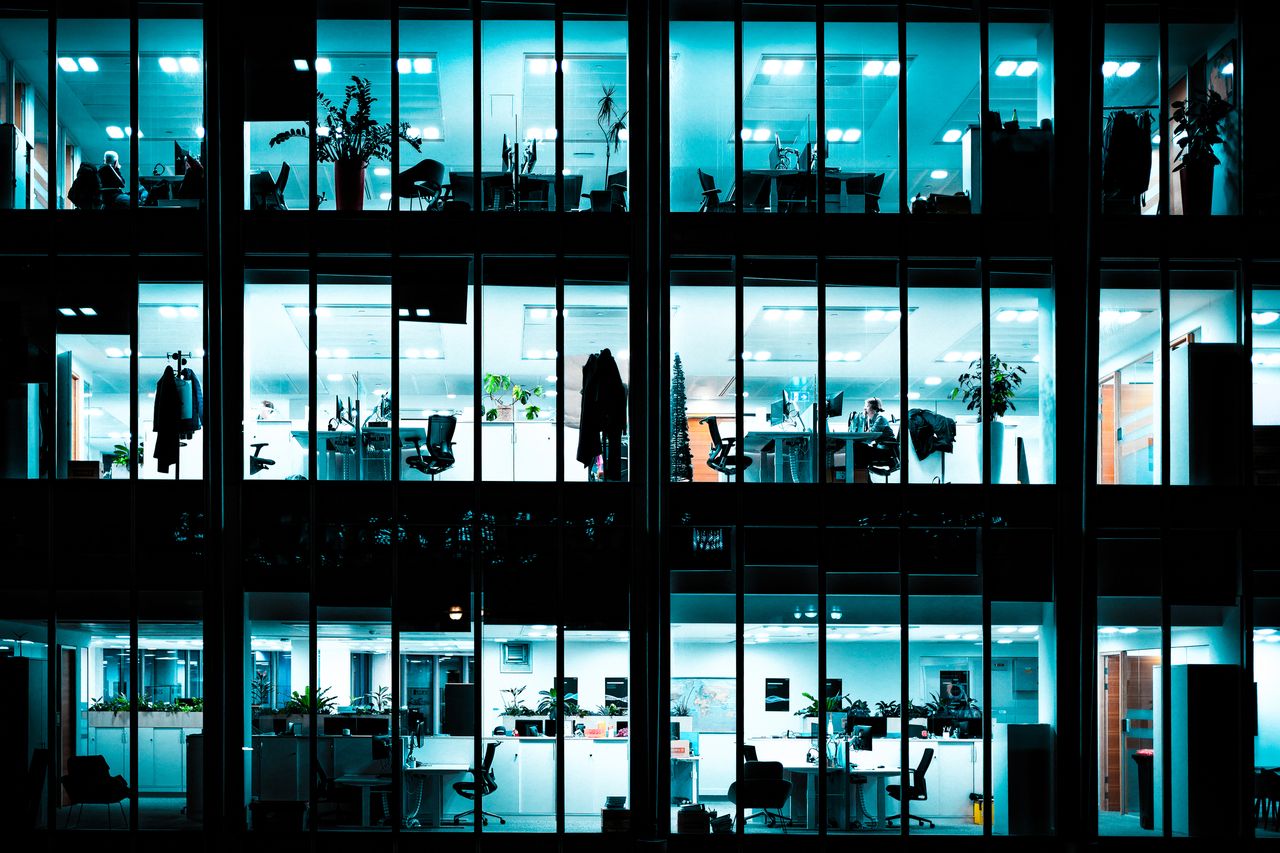 Night view of an illuminated modern office building showcasing workspaces through large windows.